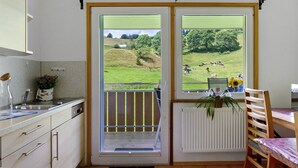 Una cucina con vista su un prato verde e delle mucche, una sedia di legno e un termosifone.