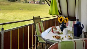 Un balcone con vista su un prato e case, un tavolo con un vaso di girasoli e una sedia.