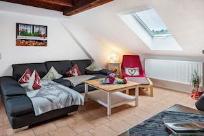 A cozy loft-style living room with a sloped ceiling, a black sofa with decorative pillows, a wooden coffee table, and a red chair.