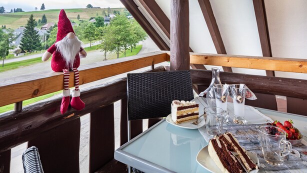 A table with a slice of cake, a glass of water, and a bowl of strawberries on a balcony with a view of a green landscape. - Holiday Apartment 'Anna' with Mountain View, Shared Terrace and Wi-Fi (Oberried-Hofsgrund)