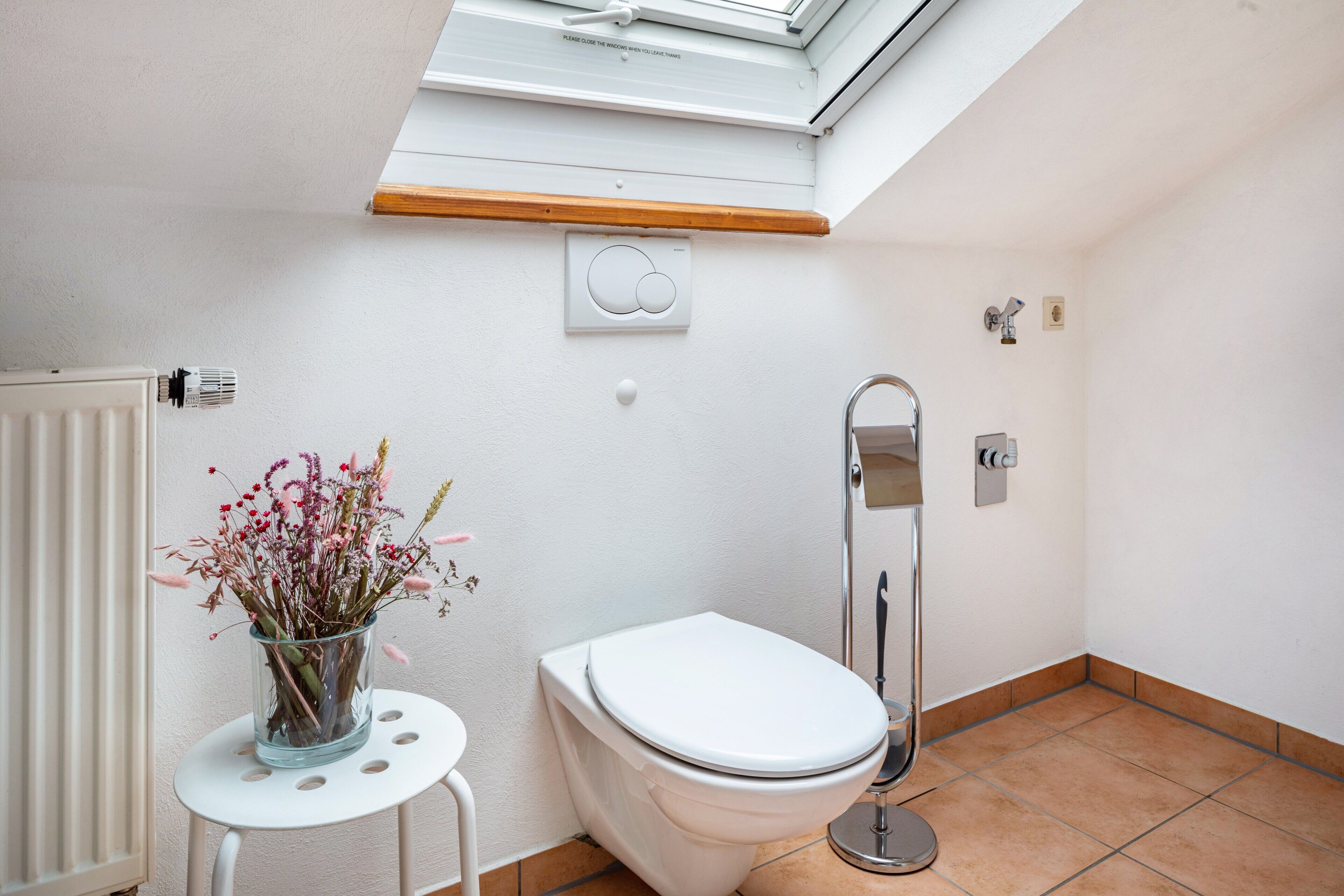 Ein Badezimmer mit Dachfenster, Toilette, Bidet und einem kleinen Tisch mit Blumen.'