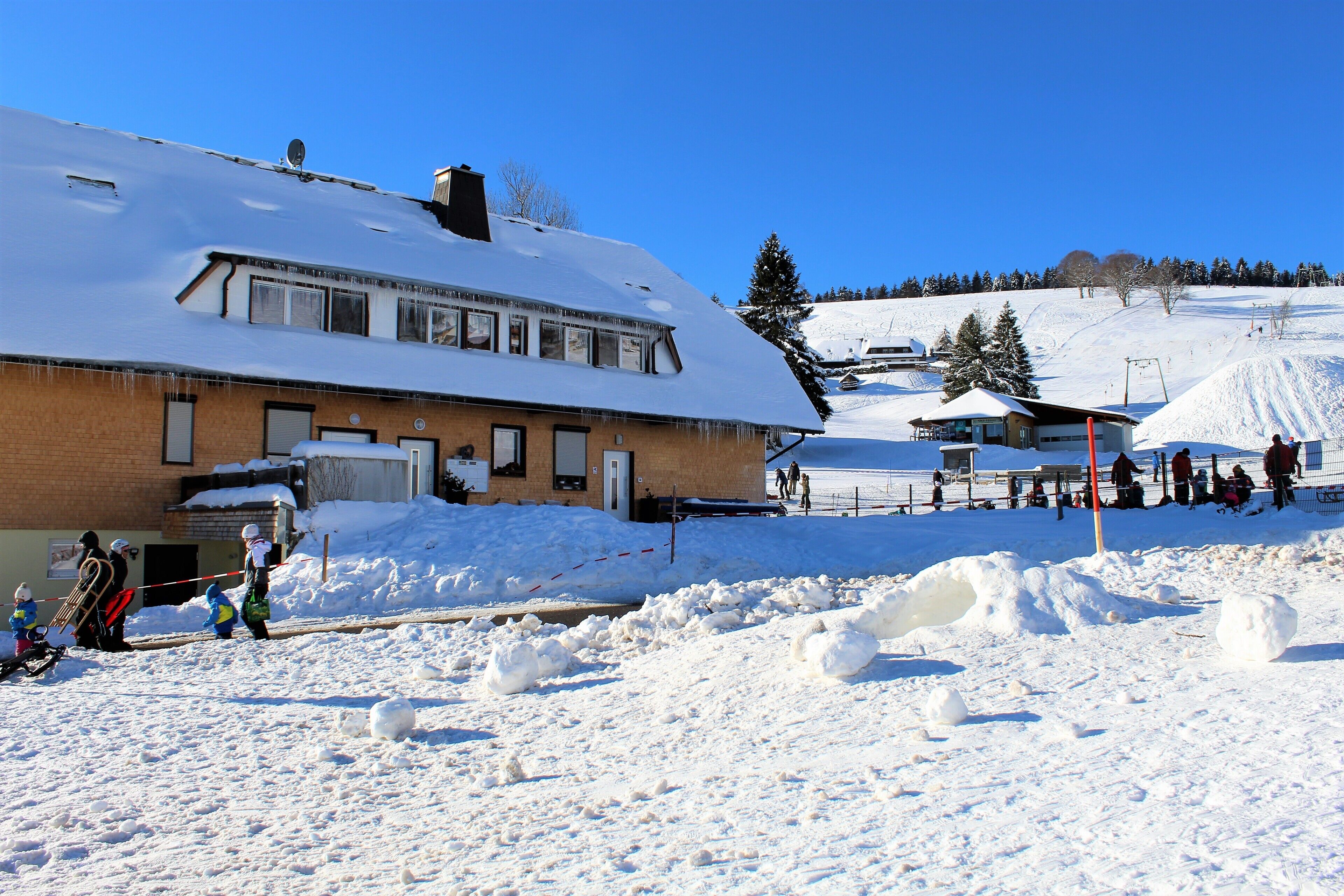 Ein schneebedecktes Gebäude mit schrägem Dach und Ziegelaußenwand, wobei eine Tür erkennbar ist.