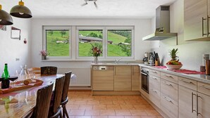 A modern kitchen with a large window, wooden cabinets, and a dining area with chairs. - Apartment 'Sport Rees - Stefanie' with Mountain View, Shared Terrace & Wi-Fi (Oberried-Hofsgrund)