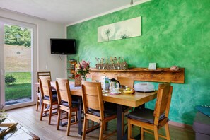 A dining area with a wooden table and chairs, a television mounted on the wall, and a green textured wall.