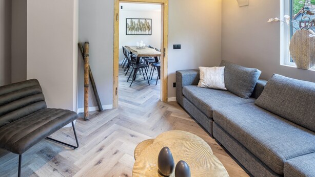 Un salon moderne comprenant un canapé, un fauteuil, un coin repas avec une table et des chaises, et une fenêtre donnant sur un beau paysage.