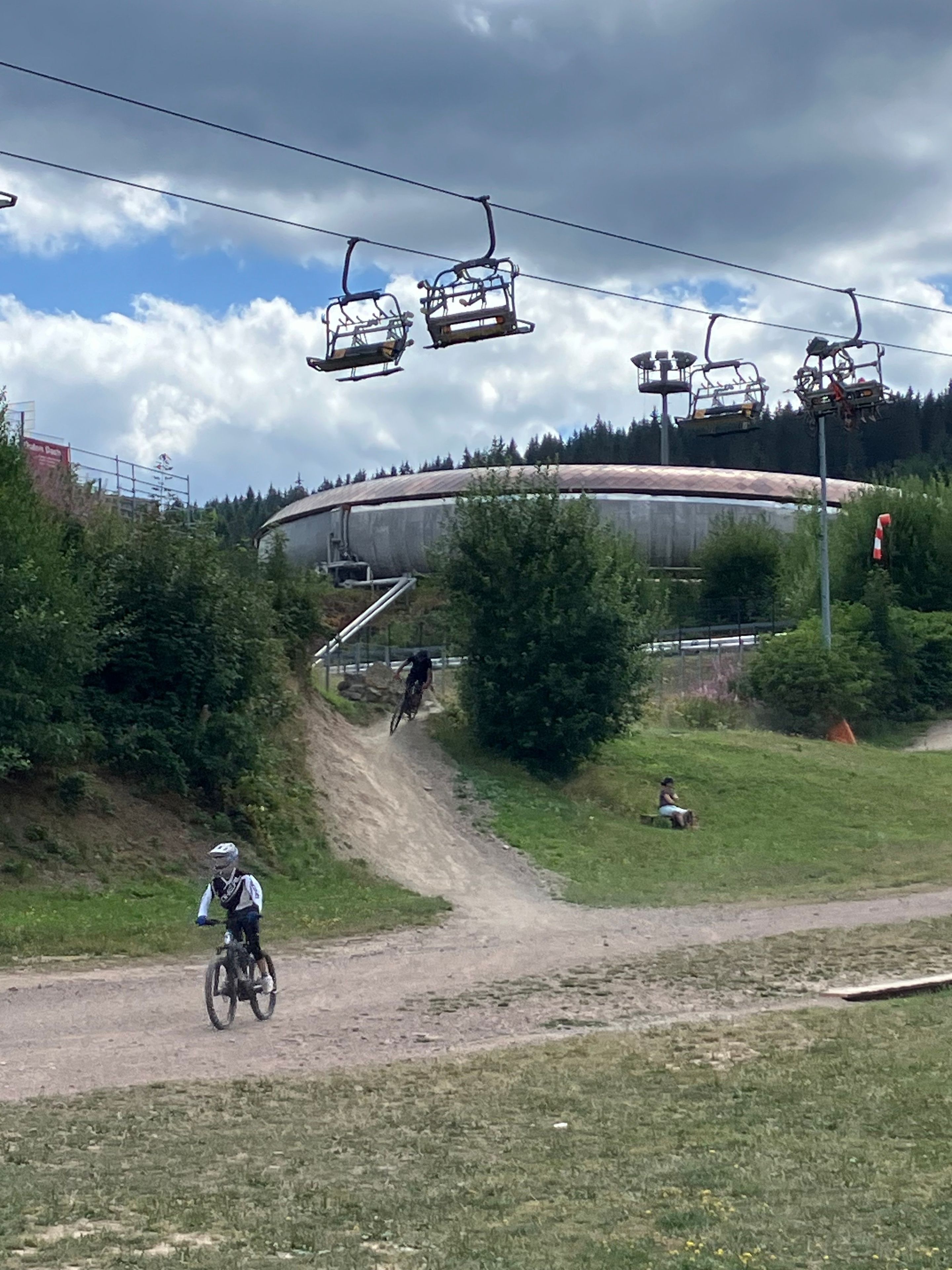 Un sender de bicicleta de muntanya amb un camí de terra, una persona anant en bicicleta i un telefèric al fons.