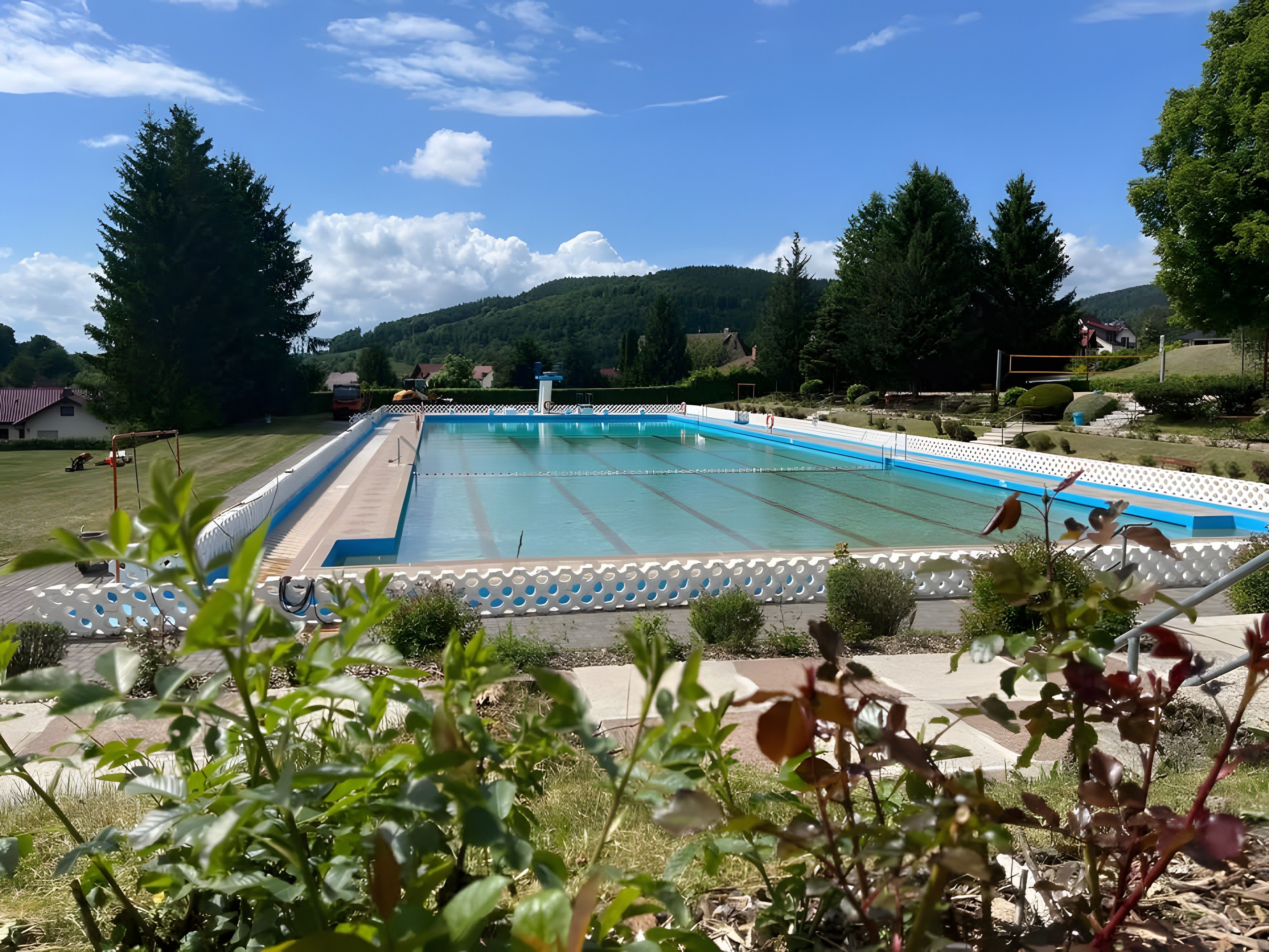Une piscine dotée d’une terrasse blanche et d’un bordure bleue, entourée de verdure et de collines.