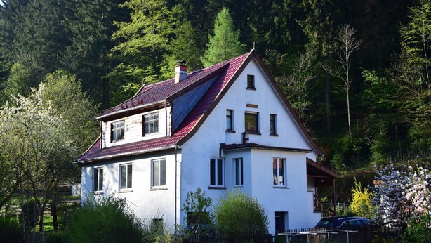 Una casa de dues plantes amb teulada vermella, envoltada d'arbres i vegetació.