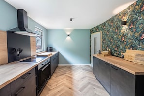 A modern kitchen with a herringbone floor, black cabinetry, and a wooden countertop. - Vacation home Haus Waldberg with large garden and covered veranda (Unterschönau)