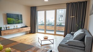 Una sala moderna con un sofá gris, una mesa de centro de madera y un televisor de pantalla plana montado en la pared.