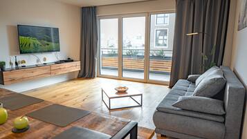 Ein modernes Wohnzimmer mit einem grauen Sofa, einem Holztisch und einem flachbildfernseher an der Wand.
