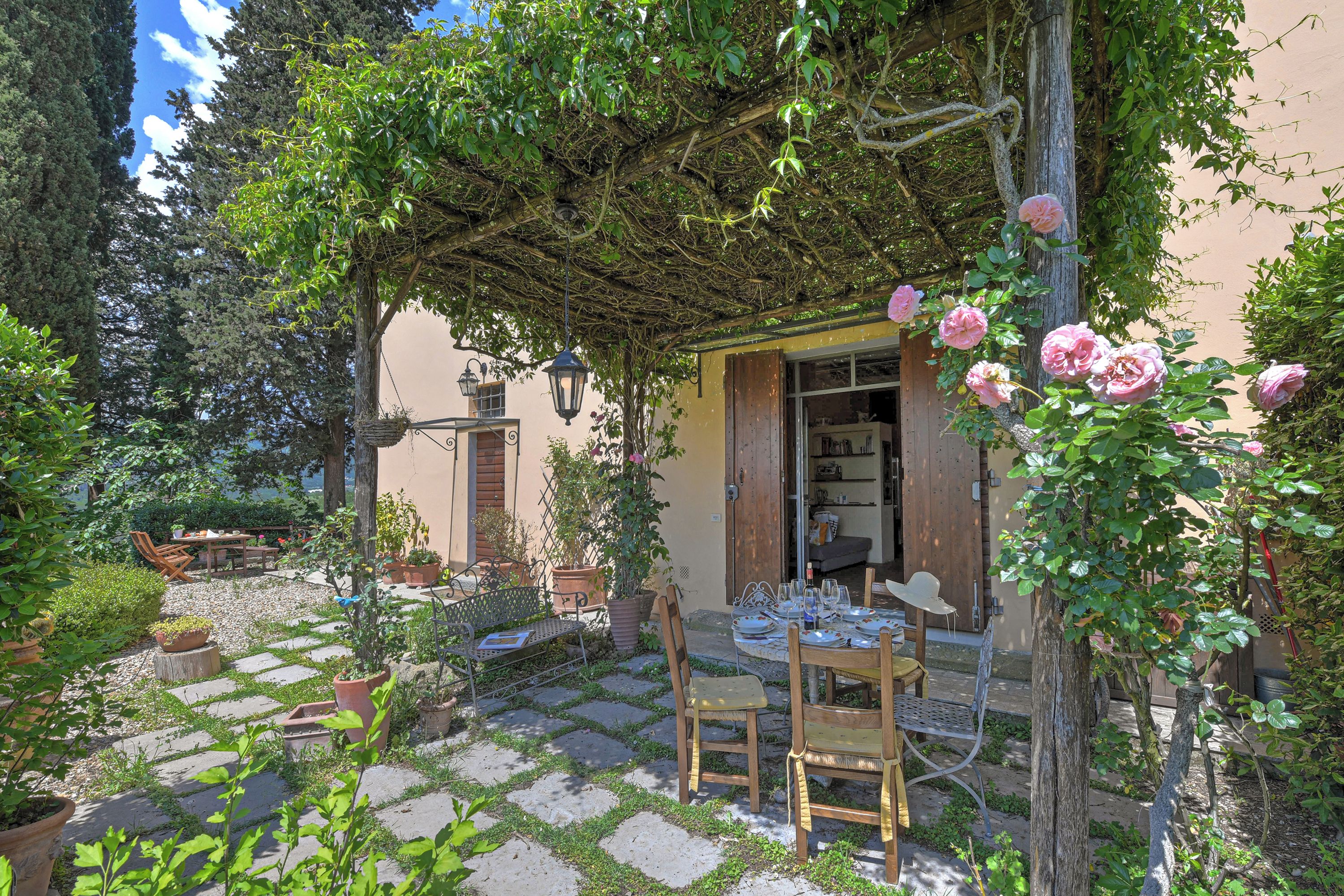 A covered patio with a table and chairs, surrounded by potted plants and a stone pathway.