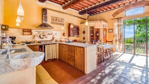 A kitchen with a marble sink, wooden cabinets, a large island, hanging lights, and a view of the outdoors through a glass door. - Tuscan Home Panoramic Hills Private Terrace (Rignano sull'Arno)
