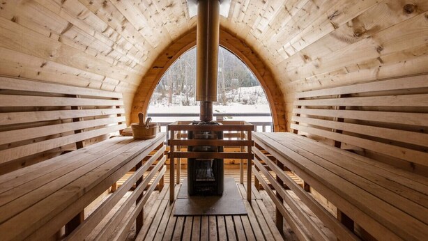 Una cabaña de madera con chimenea central, bancos y un amplio ventanal arqueado.
