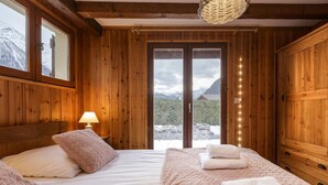 Una habitación de madera con una cama, una mesita de noche y un ventanal con vistas a las montañas.