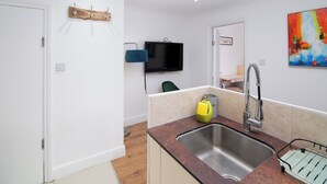 A compact kitchen with a stainless steel sink, a blue hanging light, and a television mounted on the wall.