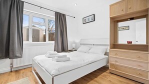 A modern bedroom with a bed, a dresser, and a window with curtains.
