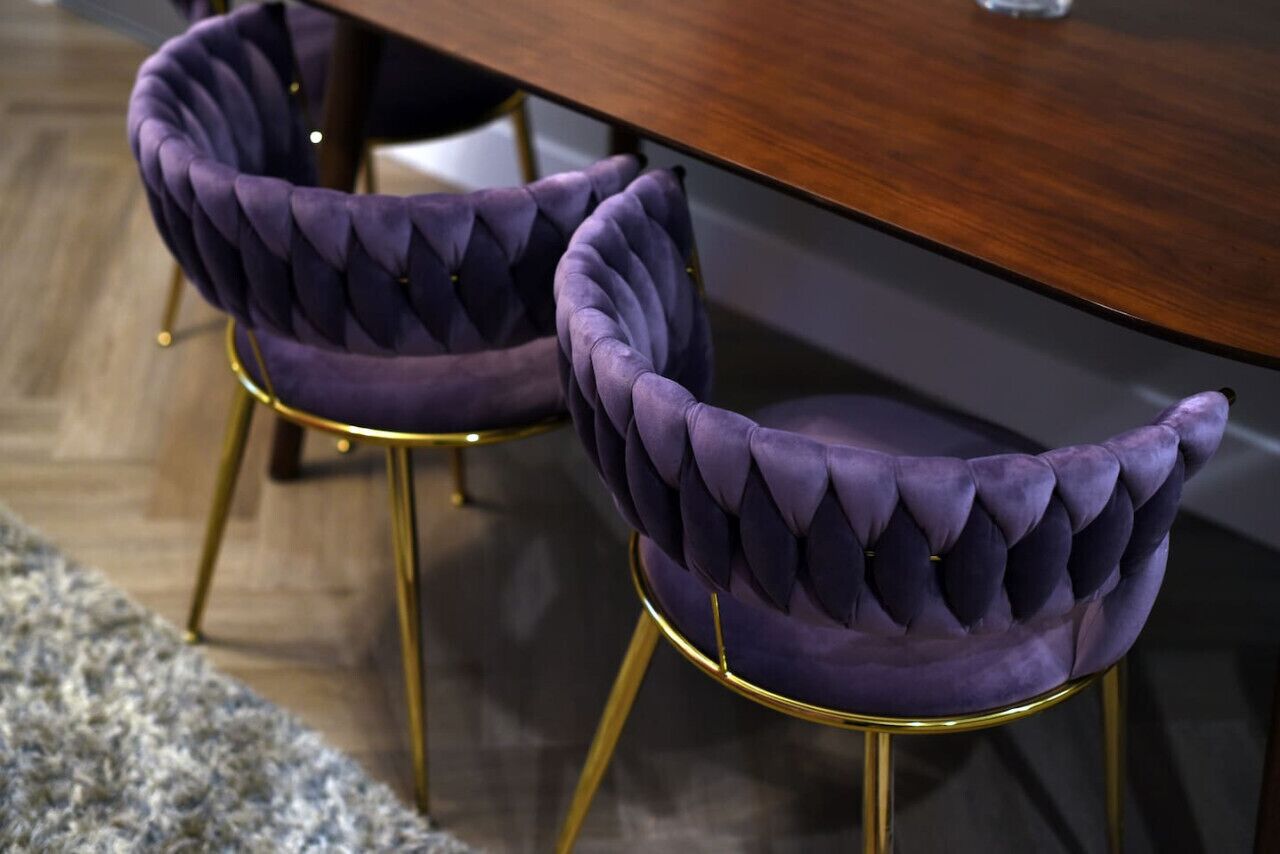 Two purple velvet chairs with gold legs and a wooden table.