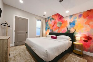 A bedroom with a bed, a bedside table, a mirror, and a colorful abstract wall. - ★ HostWise Stays ★ King Beds, Near Stadiums, Dining, Street Parking (Pittsburgh)