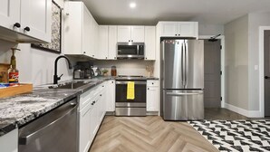 A modern kitchen with white cabinets, stainless steel appliances, and a herringbone wood floor.
