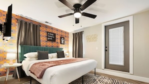 A modern bedroom with a bed, a ceiling fan, a patterned wall, and a door.