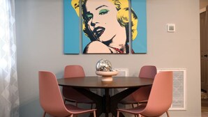 A dining area with a round table, pink chairs, and a wall-mounted artwork.