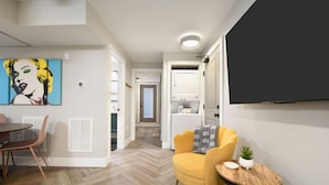 A modern living room with a dining area, a yellow armchair, a small round table, and a flat-screen TV mounted on the wall.