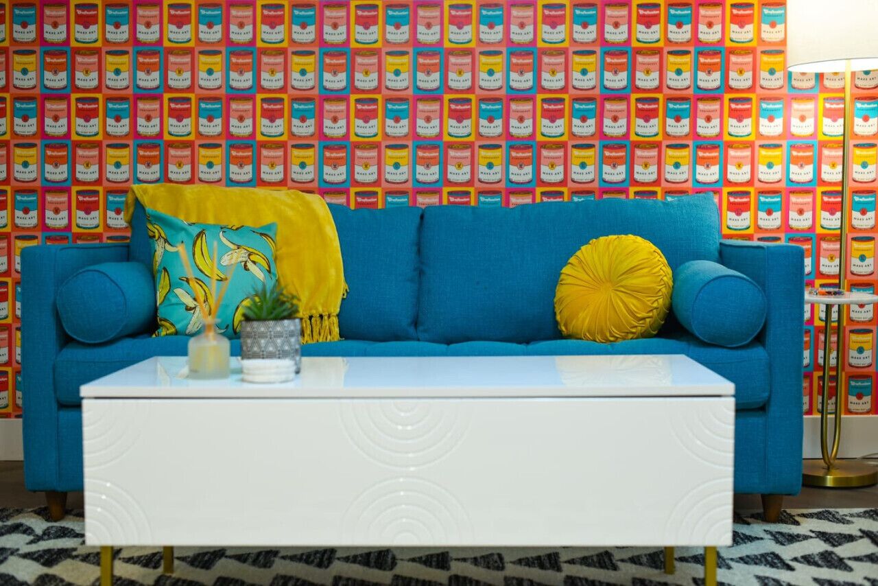 Une pièce avec un canapé bleu, une table basse blanche et des œuvres d’art colorées accrochées au mur.