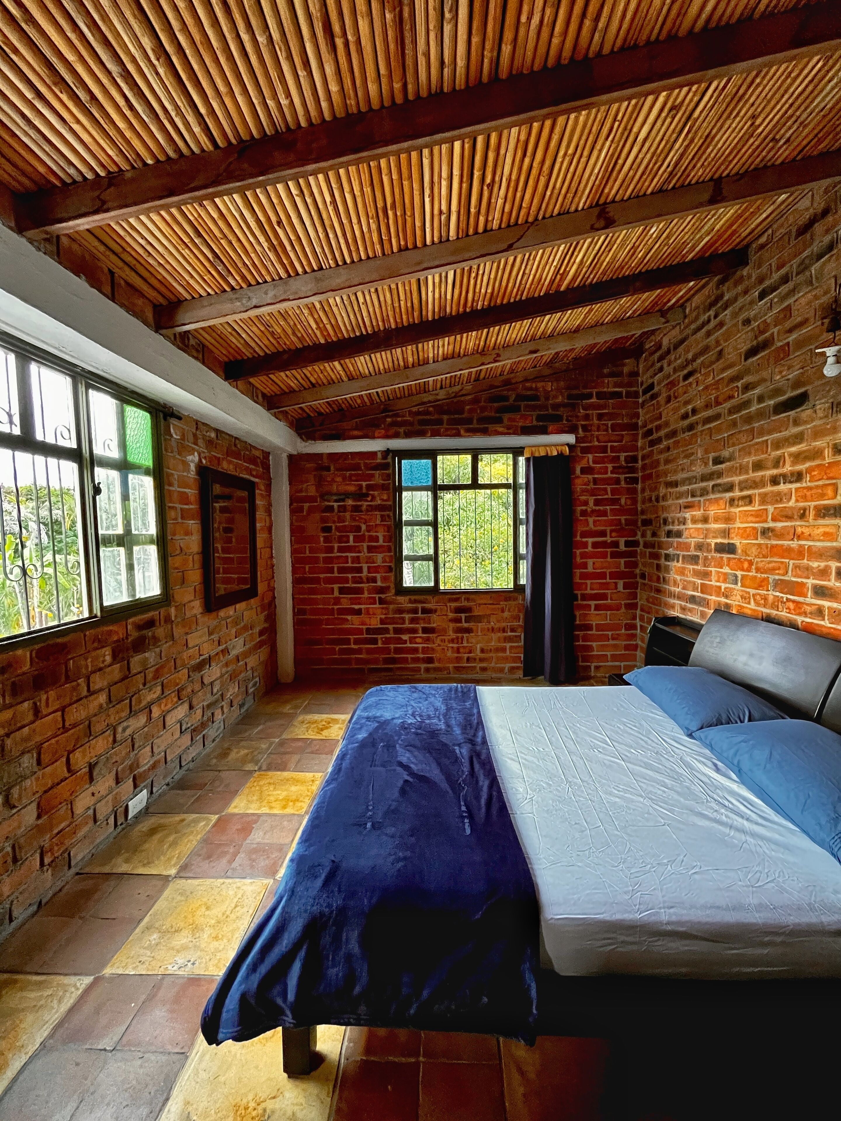 Una habitación con pared de ladrillo, cama con cubrecama azul y techo de madera.
