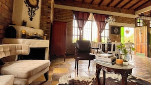 Un interior rústico con techo de madera, alfombra de cuero de vaca, una mesa de comedor con libros y un sillón de cuero.