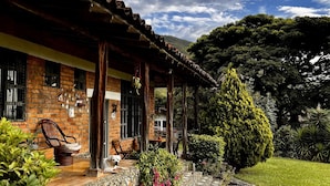 Una casa de ladrillo rústica con un porche cubierto, un sendero de piedra y abundante vegetación.