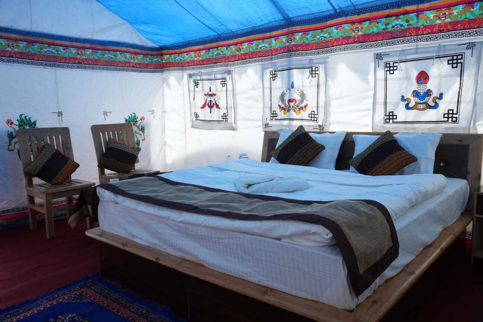 Ein traditionell eingerichteter Raum mit einem Bett, zwei Holzstühlen, einem kleinen Tisch und dekorativen Wandbildern.