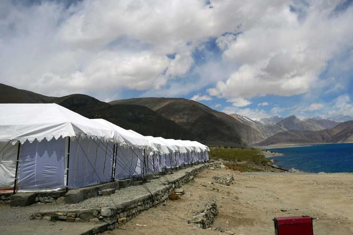 A row of white tents along a rocky shore with a lake and mountains in the background.