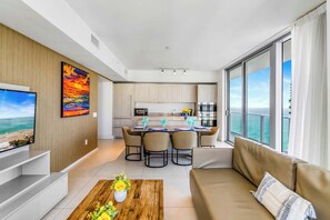 A modern living room with a sofa, a coffee table with flowers, a TV, and a dining area with chairs and a table.