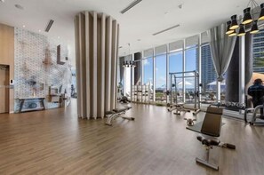 A modern gym with exercise equipment, large windows, and a brick wall.