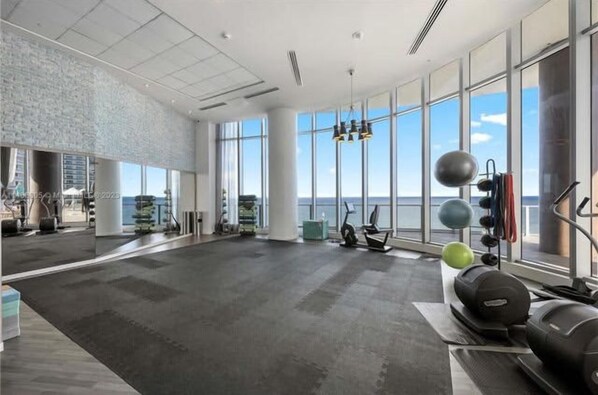 A spacious gym with large windows, exercise equipment, and a view of the ocean.