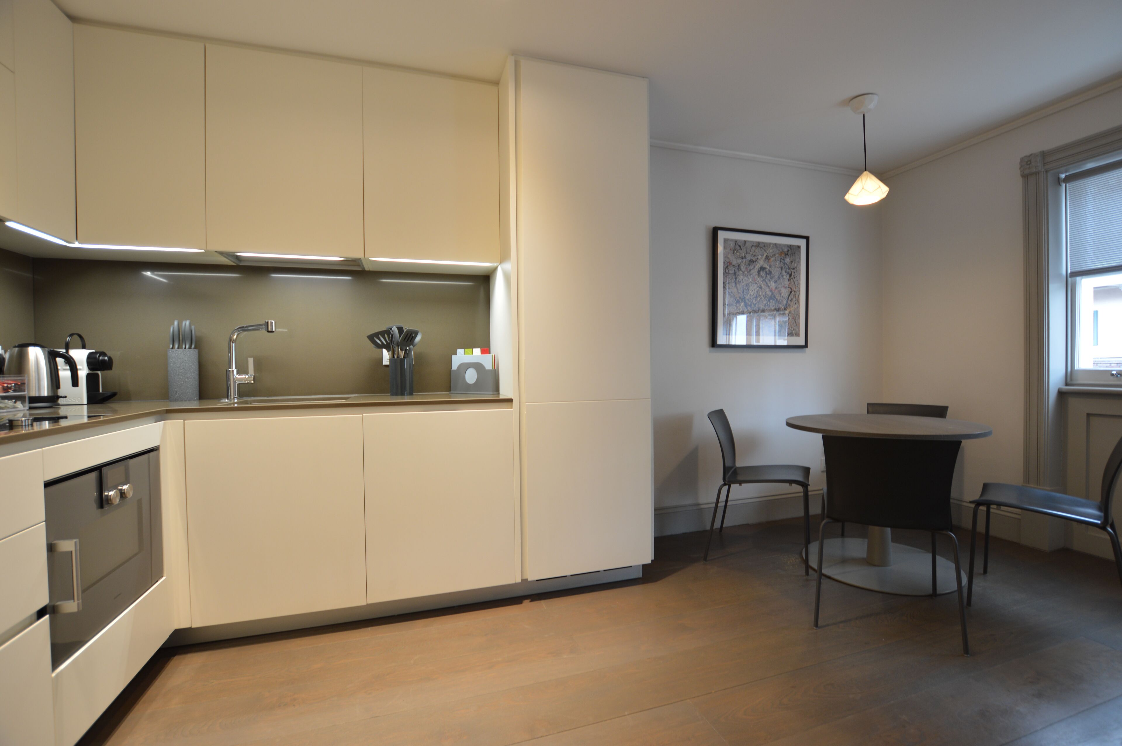 A modern kitchen with built-in appliances, a dining area with a round table and chairs, and a pendant light.