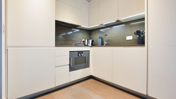 Une cuisine moderne avec des meubles blancs, un four encastré et une hotte en acier inoxydable.