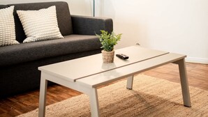A modern living room with a dark grey sofa, two white cushions, a white coffee table, a small potted plant, a floor lamp, and a framed picture on the wall. - Hamburg - 3 Rooms for up to 11 guests (Hamburg)