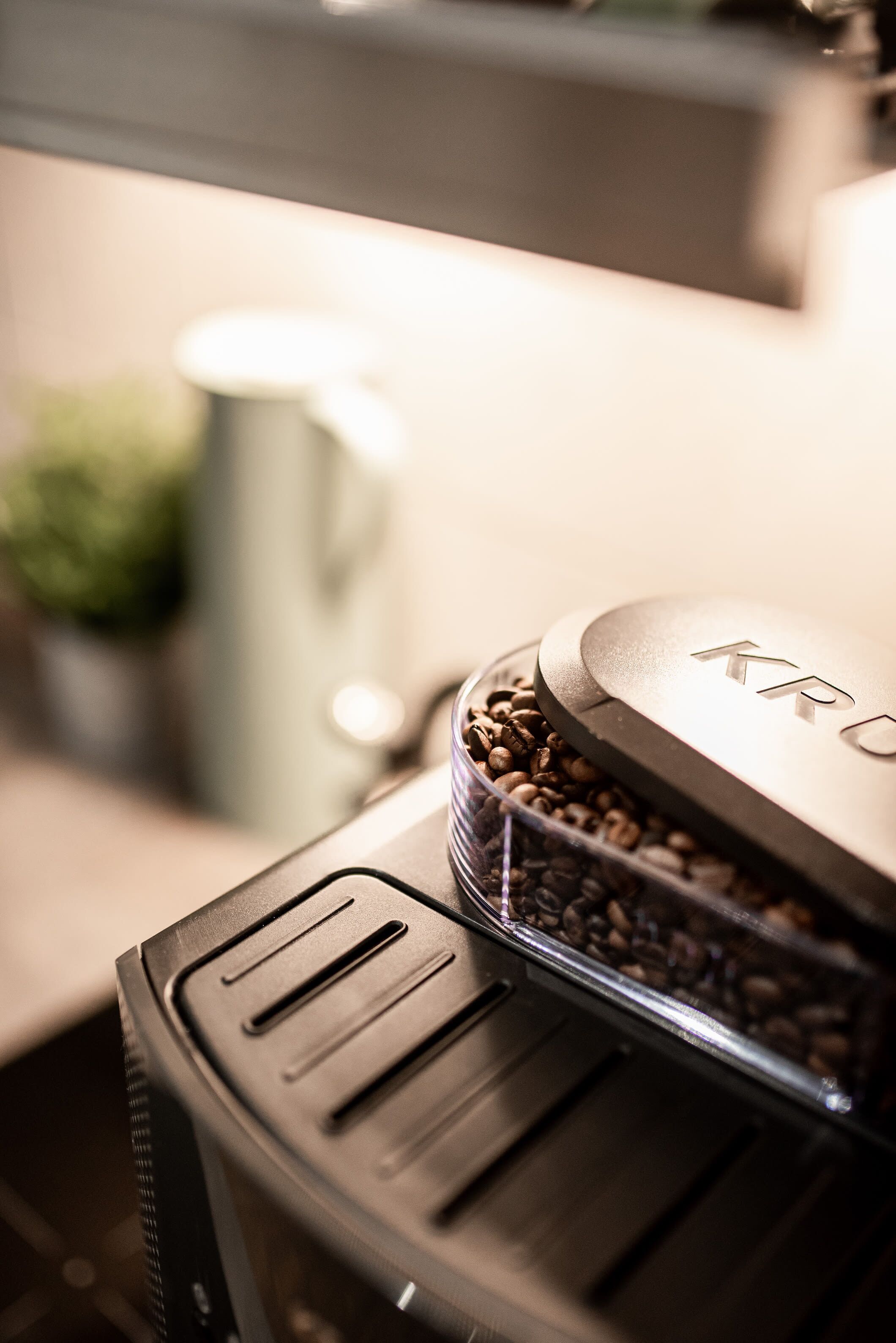 A coffee machine with a transparent container of coffee beans and a lid with the brand name "KRUPS" visible.