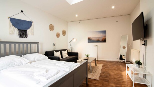 A modern bedroom with a bed, a black sofa, a desk, a mirror, and a TV. - Hamburg - 3 Rooms for up to 11 guests (Hamburg)