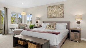 A bedroom with a large bed, a nightstand, a chair, a bench, and a window with curtains.