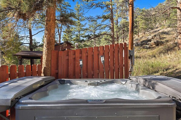 A hot tub with a wooden fence and a gazebo in a wooded area.