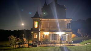 Een groot, historisch gebouw met een opvallende toren en veel ramen, met terrasjes en een verzorgd gazon.