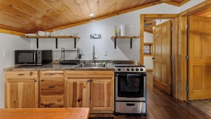 A kitchen with wooden cabinets, a microwave, a stove, and a sink. - Cabin 10- King Cabin, Mins to RMNP! (Estes Park)