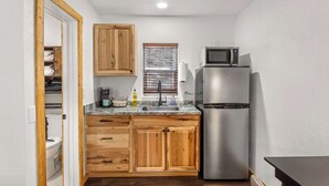 Une cuisine compacte avec des meubles en bois, un réfrigérateur en acier inoxydable, un four à micro-ondes et une fenêtre équipée de stores.