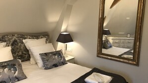 Quarto de hotel com cama, um espelho grande, mesa de cabeceira com abajur e cômoda.