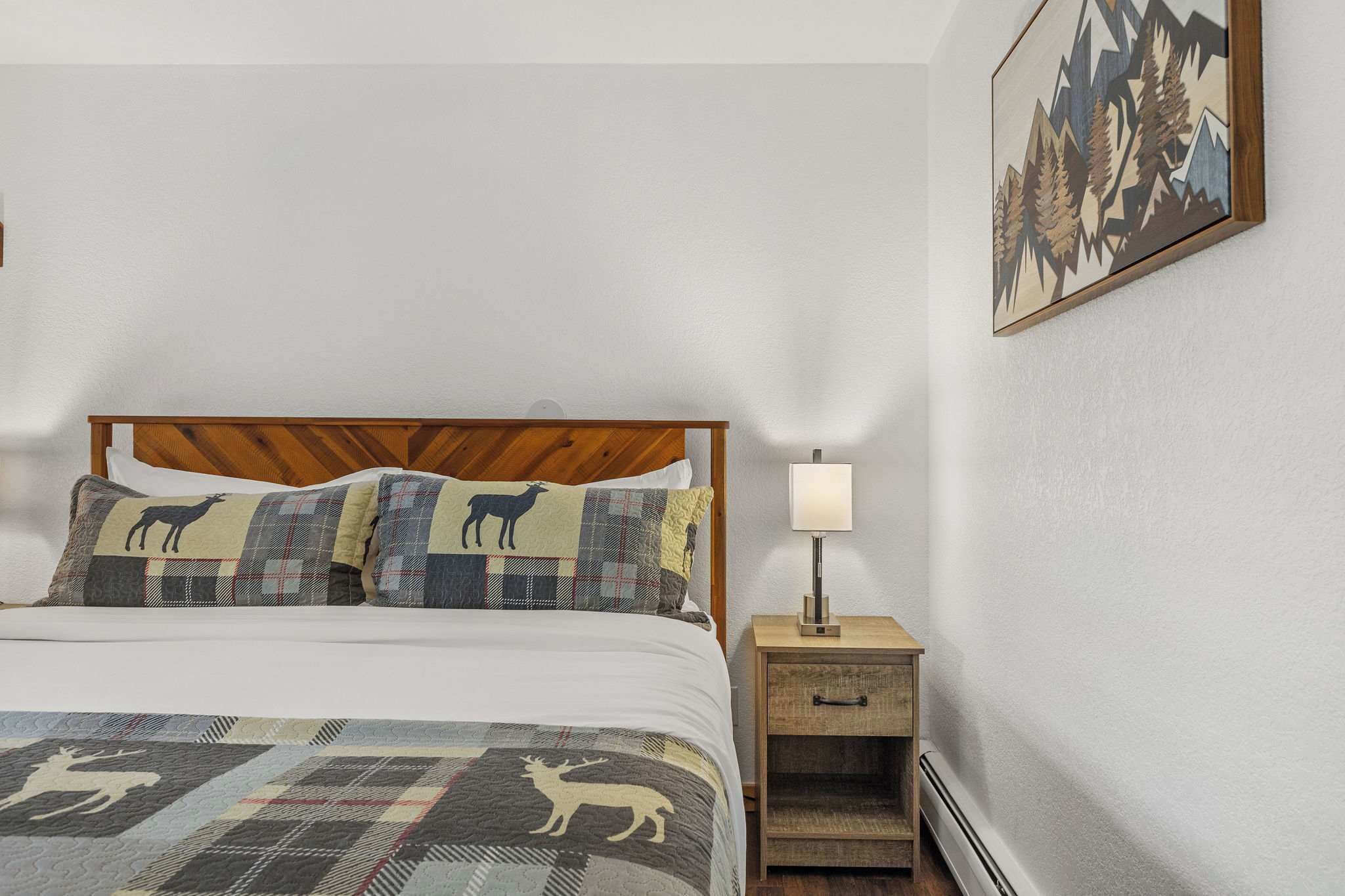 A neatly made bed with patterned pillows and a quilt, a bedside table with a lamp, and a framed picture on the wall.