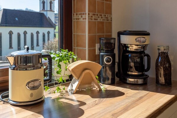 A kitchen counter with a coffee maker, a kettle, a coffee grinder, and a bottle of coffee beans.