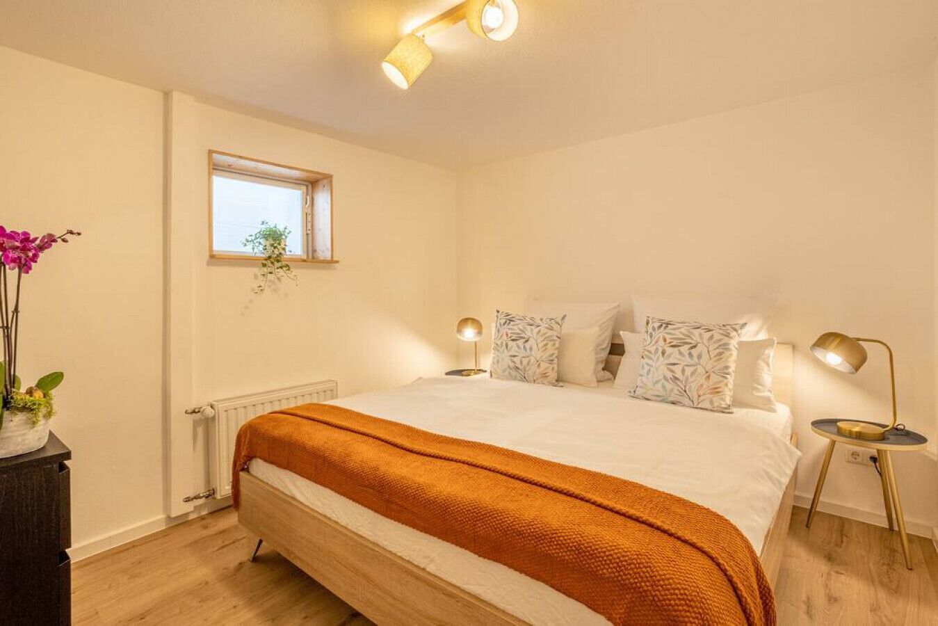A bedroom with a bed, bedside lamps, a window, and a plant.